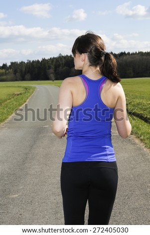 backside of a young woman jogging outdoors on the countryside