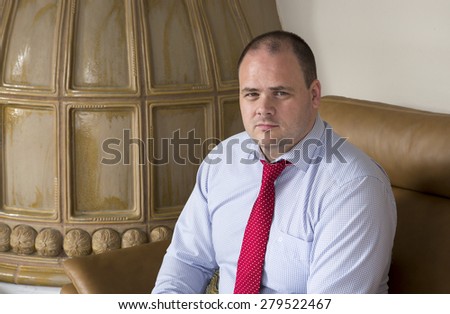 man in shirt and tie sits on couch and looks serious
