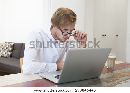 red-haired young man sitting at table and looking at his laptop