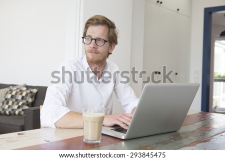 red-haired young man sitting at table with his laptop and looking thoughtfully