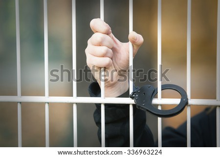 closeup of hand being handcuffed to iron bars