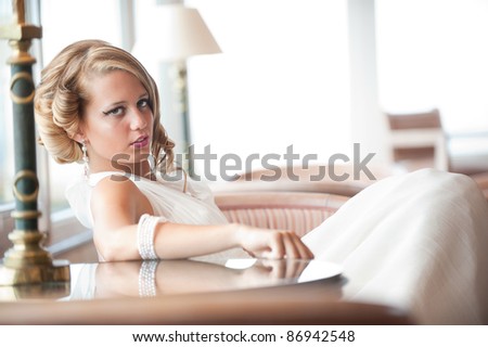 beautiful blond young woman in wedding dress seated, posing looking at the camera. Professionally done hair and makeup.
