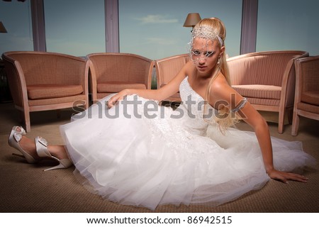 beautiful blond young woman in wedding dress seated on the floor, posing looking at the camera. Professionally done hair and makeup.