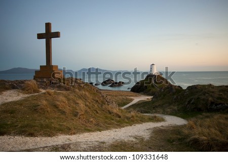 cross and lighthouse on a tidal island in wales at sunset