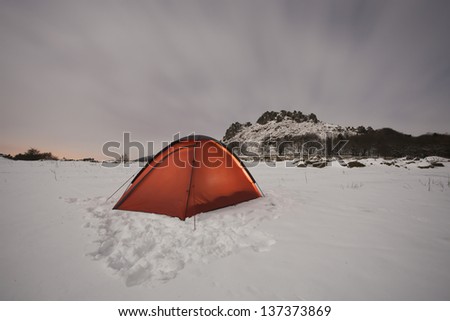 tent in the snow on in a field with mountain in the background