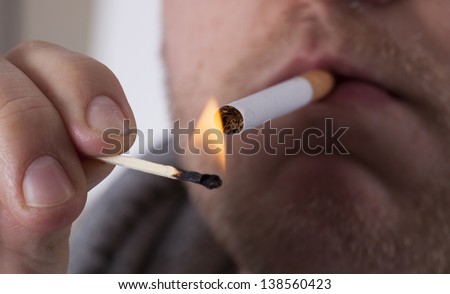 man lighting cigarette with match about to smoke