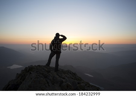 silhouette of man saluting to the early morning sunrise from a mountain top, crib goch, snowdon