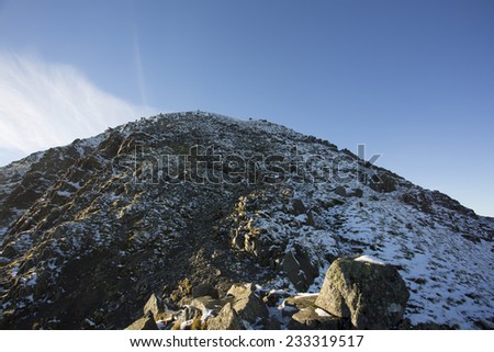 steep mountain hike covered in rocks and snow against a blue sky