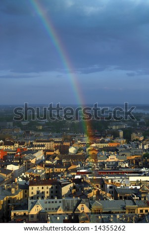 Rainbow above old european city roofs, dark clouds at background.
