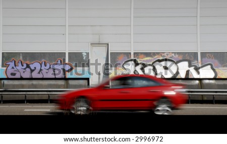 graffiti on sound isolation wall on highway with red car speeding