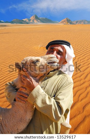 Traditional arab man kissing and hugging a baby camel in Wadi Rum desert, Jordan