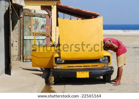 stock photo Cuban guy trying to fix his vintage american yellow car in 
