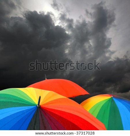 Rainbow colored umbrellas and dark cloudy sky in autumn time on square background