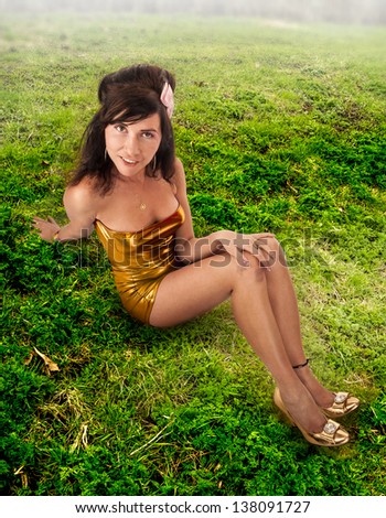 cute Latin American female sitting on a green meadow dressed in a gold dress and shoes