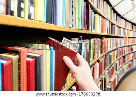 Reading/education makes you successful. Hand picking book with dollar bill in library
