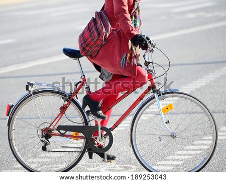 Close up of woman in red. On matching bike. Bike lane symbols on ground.