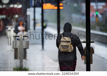 Woman in raincoat in heavy rain on train station platform