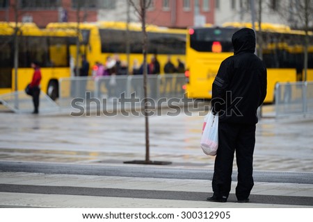Man in raincoat in rain waiting for bus