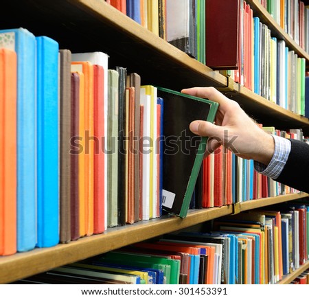 Hand picking book in library bookshelf