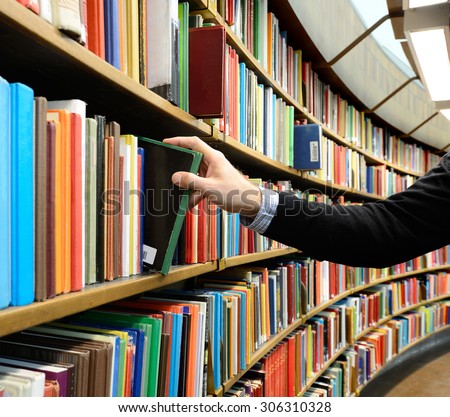 Hand picking book in library bookshelf