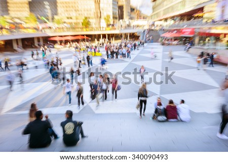 Motion and zoom blurred pedestrians crossing sunlit square. Effect made in camera, not post processing.