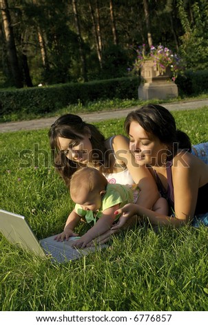 Portrait of a smiling girls on the grassy field with computer.