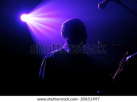 Silhouette of the playing saxophonist under beams of violet light