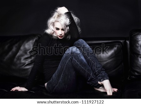 depressed platinum blonde woman on sofa. The sofa and walls are dark to reflect her state of mind.