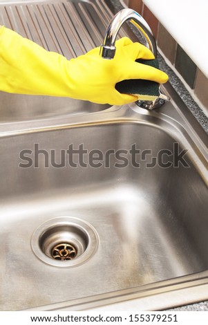 hand in a rubber glove cleaning a stainless steel sink with a sponge