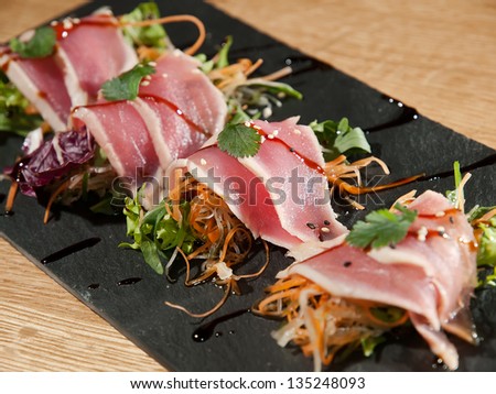Slices of prosciutto rolled up and arranged on a lettuce leaf. on a stone plate