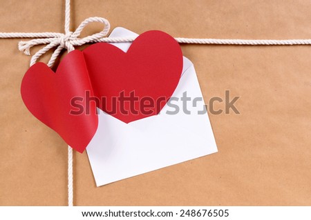 Blank red valentine card with white envelope on a brown paper package background tied with string.  Space for copy.