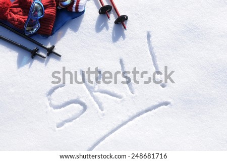 Winter skiing background with the word Ski written in snow with ski poles, goggles and hats.  Space for copy in snow.