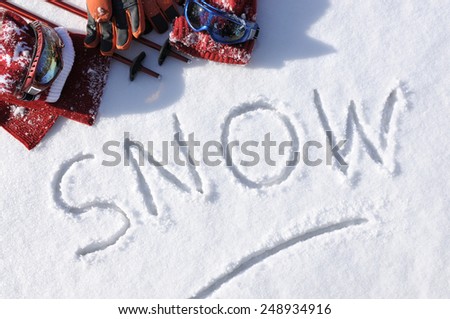 Winter sports skiing background with the word Snow written in snow with ski poles, goggles and bobble hats.