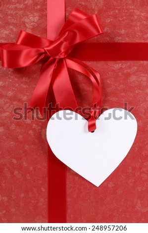 Red valentine gift background with ribbon, bow and heart shape gift tag.  Space for copy.