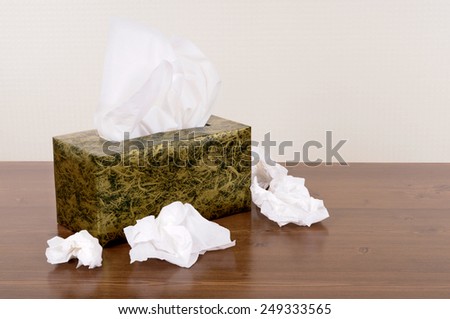 Tissue box with used tissues on a wood table.  Space for copy.