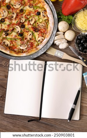 Pizza making : Freshly baked Pizza with blank recipe book or cookbook surrounded by various ingredients.  Space for copy.  Pizza cooking, pizza recipe, background.