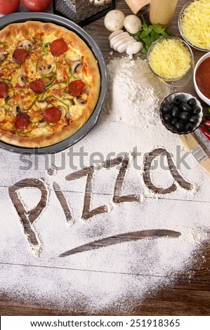 Pizza making : The word Pizza written in flour, with freshly baked pepperoni Pizza surrounded by various ingredients.  Pizza cooking, pizza ingredients.