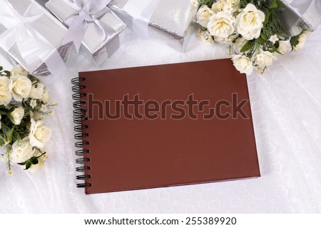 Wedding album or writing book laid on bridal lace with several silver wedding gifts and white rose bouquets.  Wedding list, record or photo album.  Space for copy.