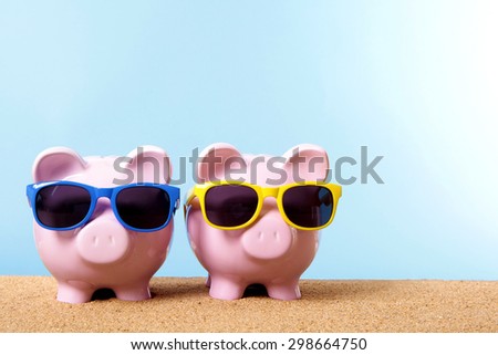 Saving money for vacation, two piggy banks on beach with sunglasses.  Copy space.