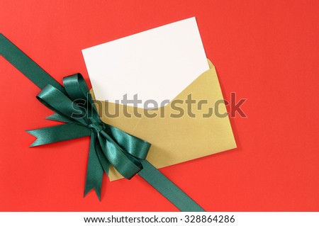 Christmas or birthday card on red gift paper background with green ribbon bow, envelope, copy space