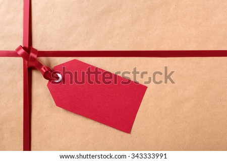 Gift tag with red ribbon, brown parcel wrapping paper background, copy space.
