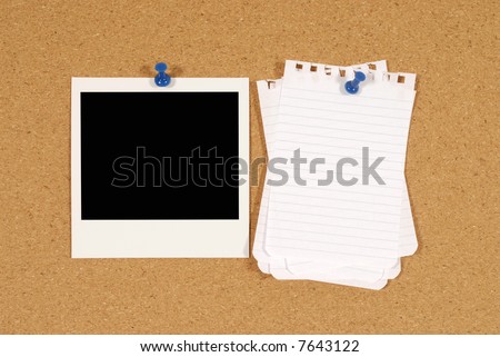 Cork notice or bulletin board with blank instant picture print and untidy notepaper.