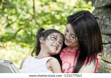 Little girl and mother enjoy tablet PC in park.