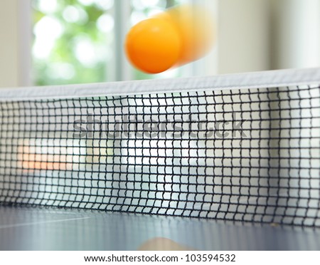 Orange table tennis ball moving over net on blue table