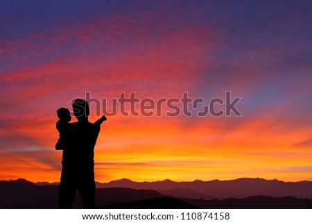 The silhouette of family (Father and child) watching the sunrise and hand finger point to sun with mountain