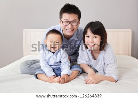 A happy family lying on white bed in the bedroom with gray wall for copy space, asian people