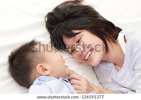 Mother And Son Smile And Look Each Other And Lying On White Bed In The Bedroom At Home, Asian Family