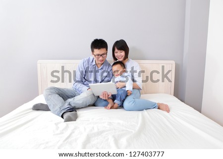 happy, family of mother, father, son sitting on bed at home having fun using a tablet pc, asian people