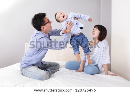 happy father hug his son with smile mother sitting on bed at home, asian family