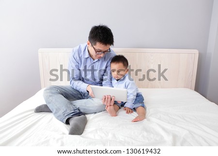 Father and son smile and happy using tablet pc on bed at home, asian people